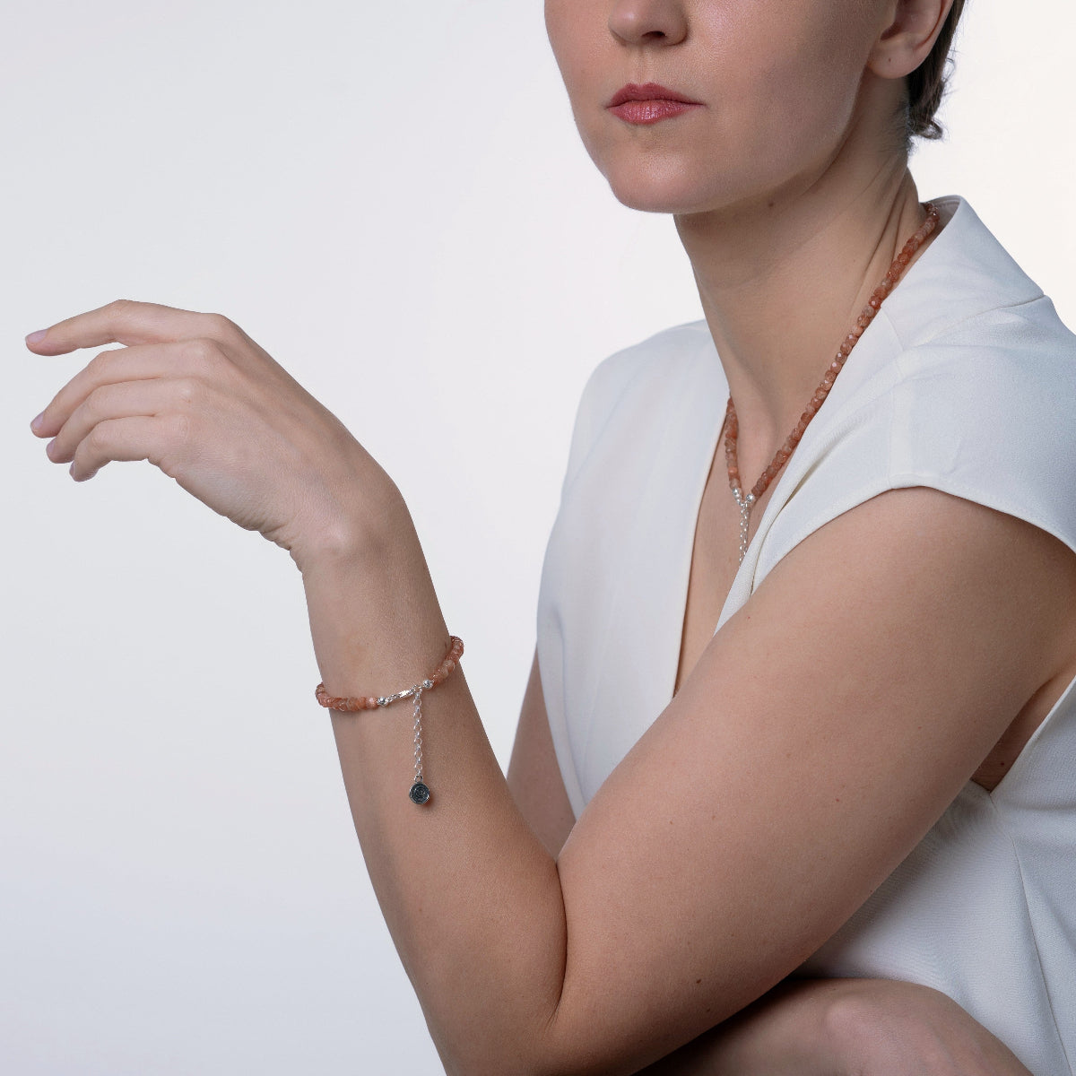 A woman wearing a delicate rose gold beaded bracelet with a small dark blue bead charm, paired with a matching rose gold beaded necklace, against a clean white background.