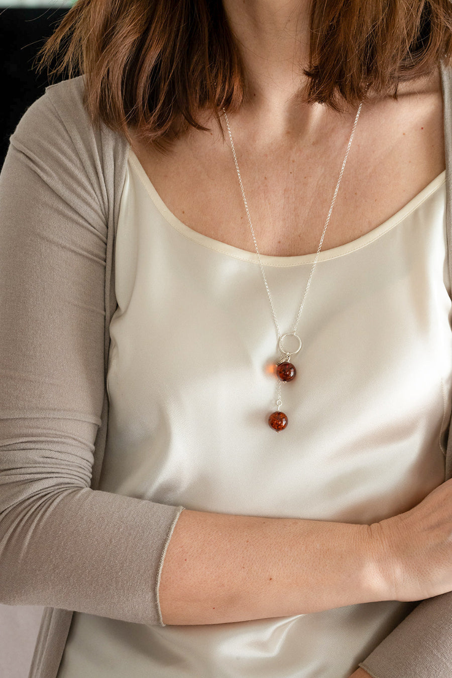 Person wearing a white satin top and a necklace with three round pendants.