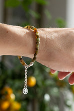 Load image into Gallery viewer, Bracelet with green and orange beads on a wrist against a blurred natural background