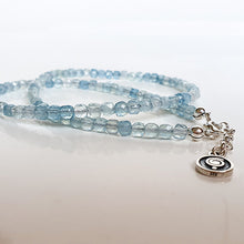 Load image into Gallery viewer, A beaded necklace with light blue aquamarine stones and a handmade silver medallion with a spiral design.