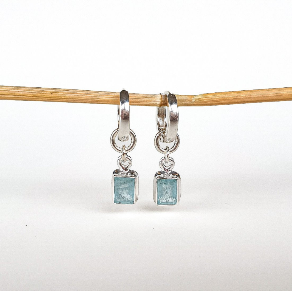 A pair of elegant silver 925 earrings featuring high-grade blue aquamarine stones, displayed against a wooden backdrop.