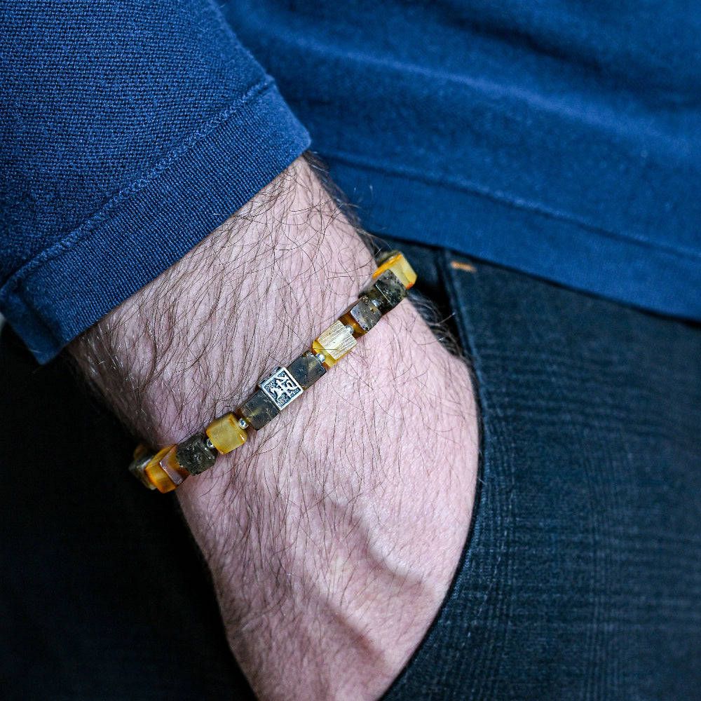 Close-up of a person wearing a beaded bracelet on their wrist with a blue shirt and dark jeans.